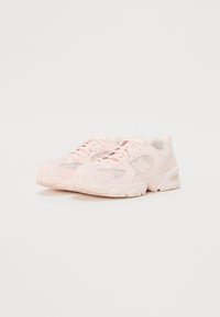 Baskets de sport rose clair avec des panneaux en mesh, des languettes rembourrées et des semelles texturées. Le design présente un logo discret et un système de laçage.