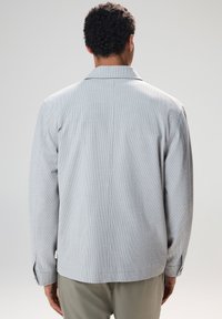 Light gray textured jacket featuring a wide collar, drop shoulders, and long sleeves with buttoned cuffs. Designed with a straight cut.