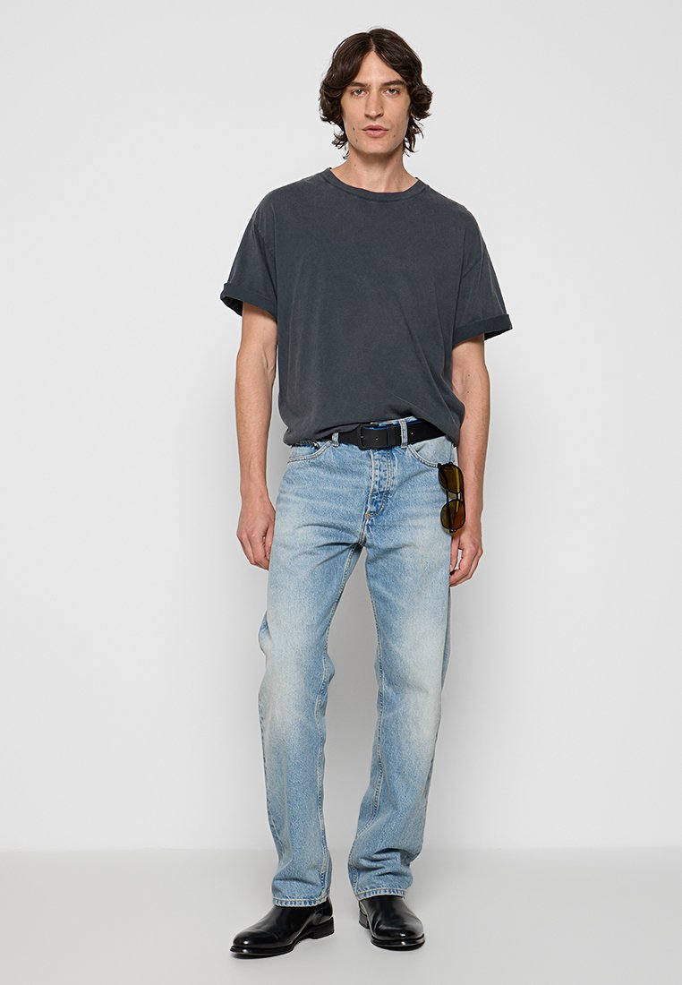 Graues, übergroßes T-Shirt, hellblaue, ausgebleichte Jeans, schwarzer Gürtel und schwarze Lederstiefel. Als Accessoires werden dunkle Sonnenbrillen getragen.