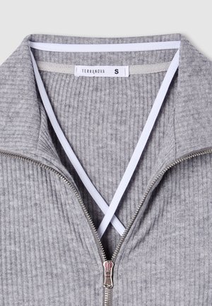 Giacca grigia a coste con zip, con un accento bianco sul colletto. Dotata di una zip argentata e un'etichetta con la scritta "TERRANOVA" e la taglia "S."