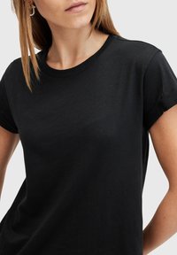 Černé bavlněné tričko s kulatým výstřihem a krátkými rukávy, s jemnou texturou a volným střihem. Žádné výrazné vzory nebo akcenty.