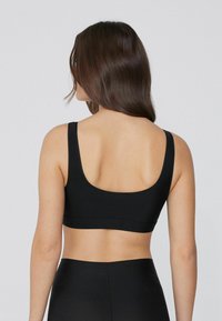 Schwarzer Sport-Bralette mit breiten Trägern, einer runden Rückenpartie und nahtlosem Design. Hergestellt aus glattem, dehnbarem Material für mehr Komfort.