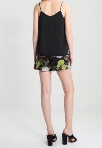 Camisola in satin nero con spalline sottili, abbinata a pantaloni corti con motivo floreale in colori vivaci. Modella che indossa sandali a blocco neri.