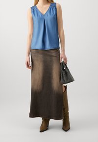 Sininen ilman hihoja paita, jossa on V-pääntie, yhdistettynä pitkään ruskeaan ombre-hameeseen. Teksturoitu käsilaukku ja polven korkeudelle ulottuvat vaaleat saappaat viimeistelevät asun.