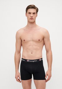 Sorte boxer shorts laget av bomull med en glatt tekstur. Har en merkebånd i elastisk stoff i hvitt og rødt, med en tettsittende design.