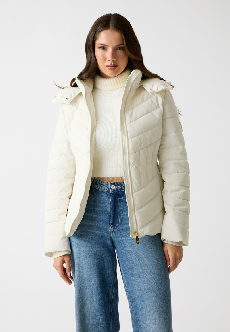 Giacca puffer bianca con zip frontale, colletto strutturato e design trapuntato. Abbinata a un maglione crema e jeans a gamba larga azzurri.