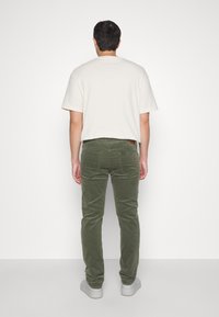 Pantalones de pana verde con un corte ajustado, combinados con una camiseta de manga corta beige claro. Textura suave y diseño minimalista.