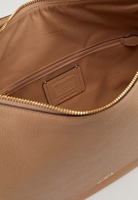 Brown leather bag interior with a gold zipper; features a zippered pocket, fabric lining, and a branded leather tag.