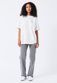 Witte oversized t-shirt met een blauwe graphic, gecombineerd met grijze flared jeans en witte sneakers. De stof lijkt soepel en ontspannen.