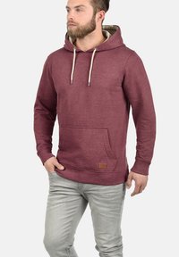 Sudadera con capucha color marrón oscuro, con un bolsillo tipo canguro, cordones crema y una pequeña etiqueta de cuero marrón en el dobladillo; material de mezcla de algodón.