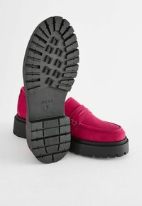 Mocasini din suede fucsia cu vârf rotund și talpă din cauciuc negru, având modele profunde de profil. Logo-ul brandului imprimat pe talpă.