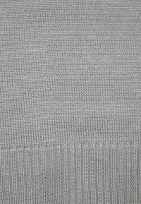 Tissu tricoté gris avec une texture uniforme, comportant à la fois des points de couture lisses et des accents côtelés au bord inférieur.
