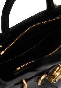 Intérieur d'un sac à main en cuir noir avec une fermeture éclair dorée et des détails en métal doré sur les poignées.