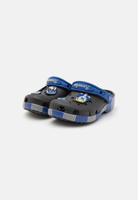 Black clogs with blue accents and gray striped soles. Features decorative patches on the upper and ventilation holes for breathability.