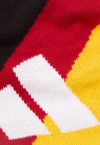 Κοντινή λήψη πλεκτού υφάσματος με γεωμετρικά μοτίβα σε μαύρο, κόκκινο, κίτρινο και λευκό χρώμα, με σφιχτές και ομοιόμορφες ραφές.