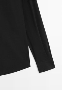 Černá košile s dlouhým rukávem a hladkým povrchem, s ohrnutým manžetou a jemným zakřiveným lemem na dolním okraji.