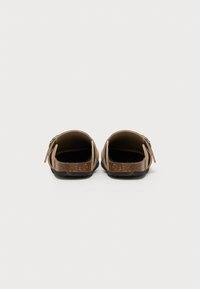 Brown sandals with open back, textured cork footbed, adjustable strap, and rubber sole. Features sleek design and neutral color scheme.