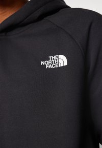 Sudadera negra de tejido suave con un logo blanco de The North Face en el lado superior izquierdo. Textura lisa, diseño minimalista.