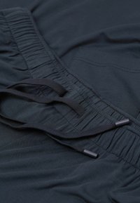 Donkerblauwe broek met een elastische tailleband met geraffineerde textuur en zwarte trekkoorden. De stof lijkt zacht en lichtgewicht te zijn.