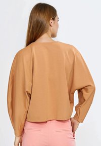 Brązowy, oversize’owy sweter z okrągłym dekoltem i opuszczonymi ramionami, z długimi rękawami i gładką fakturą tkaniny.