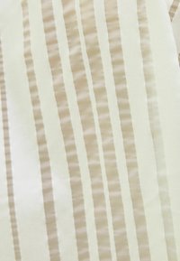 Kermanvärinen kangas, jossa on vuorotellen kiiltäviä ja mattapintaisia pystysuoria raitoja. Hento tekstuuri tuo syvyyttä; sileä pinta korostaa suunnittelun eleganssia.