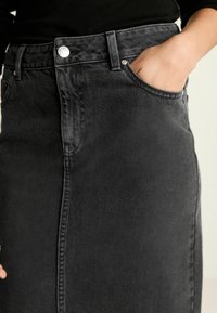 Falda de mezclilla negra con corte recto, bolsillo frontal y detalles de costura visibles. Presenta un cierre con botón metálico en la cintura.