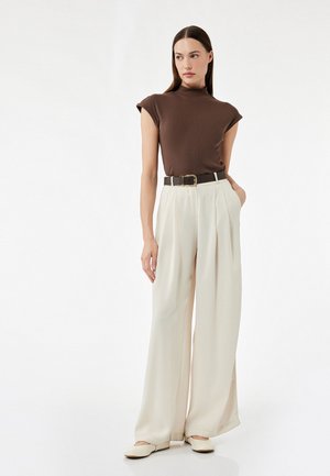 Top marrón de manga corta con cuello alto, pantalones anchos blancos y un cinturón oscuro con una hebilla dorada. Textura de tela suave.