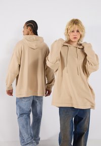 Beige oversized hoodies with drawstrings, featuring dropped shoulders, paired with loose-fit denim jeans in varying blue shades.