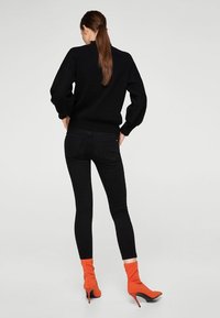 Suéter negro de punto con mangas abullonadas, combinado con jeans ajustados negros y botas calceta naranjas de tacón alto.