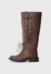 Stivale alto in finta pelle marrone con tre fibbie regolabili e lacci frontali. Suola resistente con un leggero tacco e dettagli di cucitura decorativa.