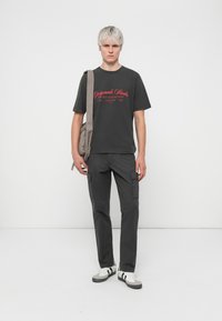 Tricou din bumbac gri cu text roșu, asortat cu pantaloni cargo gri. La ținută se adaugă adidași albi cu accente negre.