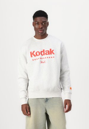 Sudadera gris hecha de una mezcla de algodón, con un gran logo rojo de "Kodak" y el texto "Huf". Mangas con puños y un pequeño parche de logo en la manga.