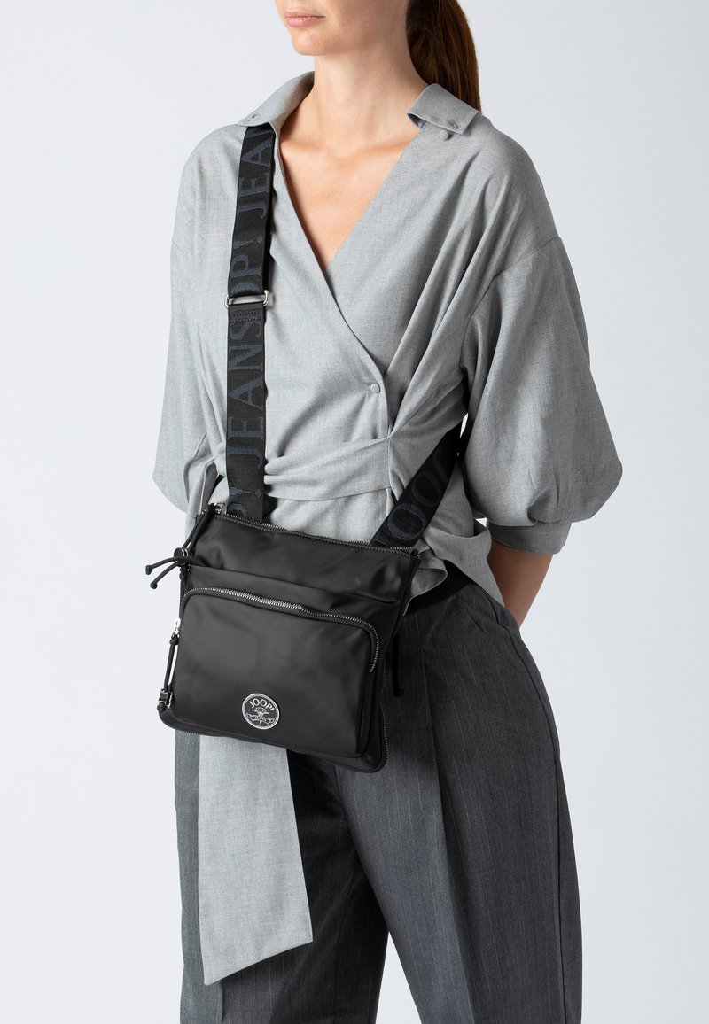 Borsa a tracolla nera con finitura liscia, dotata di una patch con logo, due scomparti con zip e una tracolla regolabile con stampa del logo.