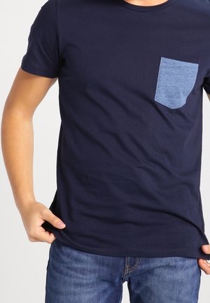 Granatowa bawełniana koszulka z jednolitym kolorem i jasnoniebieską dżinsową kieszenią po lewej stronie. Krótkie rękawy i okrągły dekolt.