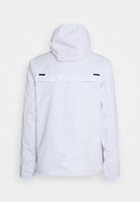 Chaqueta blanca impermeable con capucha, que presenta detalles en negro y un diseño simple y limpio. La vista trasera muestra costuras planas y sin fijaciones visibles.