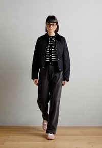 Veste noire matelassée avec un col, sur un top à rayures noir et blanc, associée à un pantalon gris ample et des baskets rose pâle.