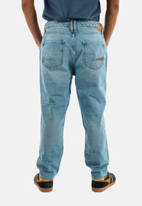 Jeans de mezclilla de color azul claro con un corte relajado, cinturilla elástica y dos bolsillos en la parte trasera, combinados con zapatos oscuros que tienen acentos naranjas.