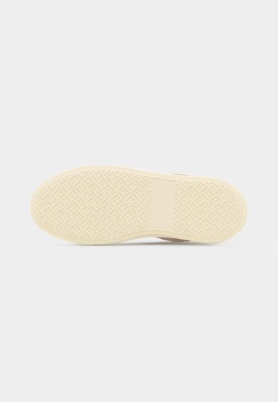 Σόλα μπεζ αθλητικού παπουτσιού με υφή γεωμετρικού πέλματος και ορθογώνιο λογότυπο στο κέντρο σε λευκό φόντο.