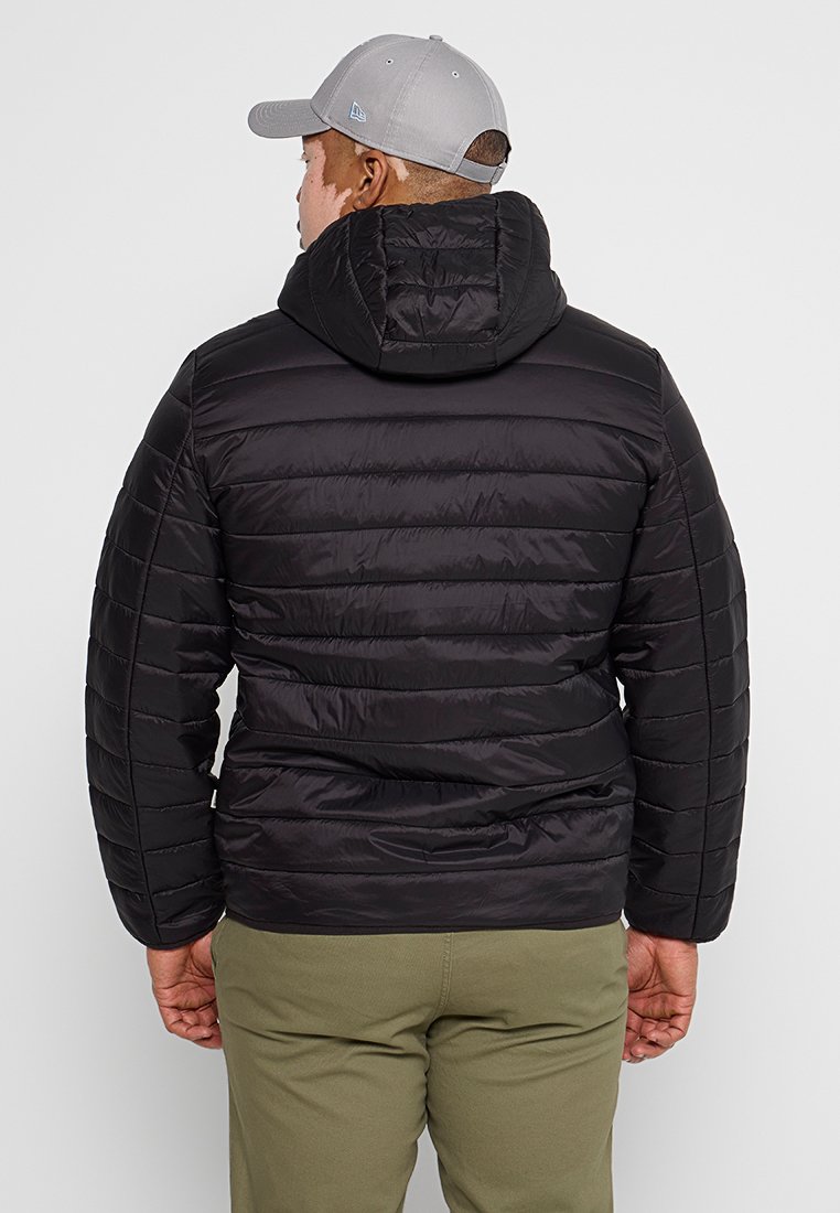 Giubbotto piumino nero con cuciture orizzontali e cappuccio, indossato sopra pantaloni verde chiaro. Presenta una texture liscia e lucida.