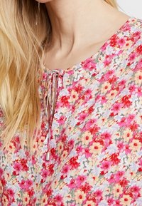 Blusa floral con tejido ligero, patrón de flores multicolores, cuello redondo con detalle de lazo y corte relajado.