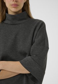 Harmaa, korkea kaula-aukko pullover, jossa on kolmanneksen mittaiset hihat. Pehmeä, tekstuuriainen kangas, jossa on rento istuvuus. Minimalistinen muotoilu, ei kuvioita tai koristeita.