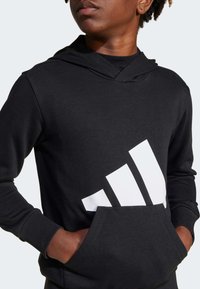 Schwarzer Hoodie mit Kängurutasche, der ein auffälliges weißes Adidas-Logo sowie gerippte Bündchen und Saum aufweist. Hergestellt aus einer weichen Baumwollmischung.