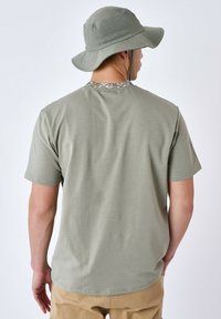 T-shirt oliva a vestibilità ampia con maniche corte, realizzato in materiale morbido. Presenta una rifinitura decorata sul colletto ed è abbinato a un cappello a secchiello coordinato.