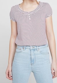 Stribet kortærmet top i lys pink og burgundy, med rund hals og diskret samling ved brystet. Sættes sammen med lys blå jeans.