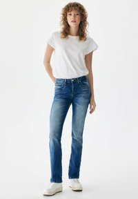 Modre denim hlače ravnega kroja z zbledelim zaključkom, v kombinaciji z enostavno belo majico. Obleka vključuje bele superge za sproščen videz.