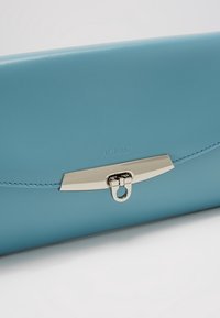 Ljusblå läderplånbok med en elegant, slät yta, utrustad med ett metallspänne med en cirkulär öppning och präglad "PICARD"-logotyp.