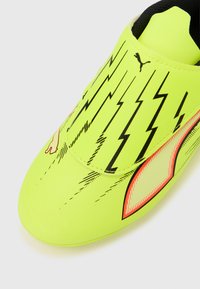 Neongul fodboldstøvle med sorte lyn grafik, en glat syntetisk overdel og en tekstureret orange detalje på siden.