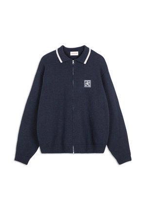 Navy knit cardigan with a zip front, ribbed cuffs, and collar. Features a white striped collar and a square patch on the chest.