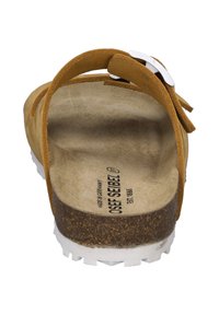 Bruine suède sandaal met een kurken voetbed, verstelbare gespsluiting en witte rubberen zool; textuur binnenin voor grip en comfort.