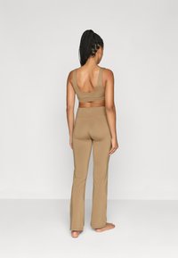 Καστανό seamless αθλητικό σουτιέν και φαρδιά κολάν, με λεία υφή και φαρδιές τιράντες, απεικονιζόμενα από πίσω σε ουδέτερο φόντο.